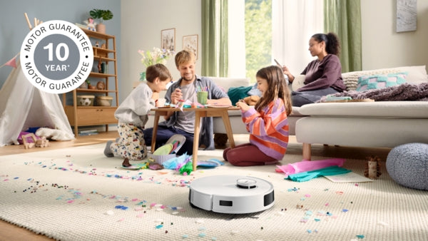 White Bosch BCRD2W robot vacuum cleaning a beige carpet in a family living room with children playing in the background.