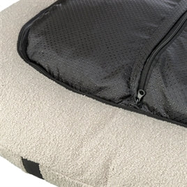 Oval cream dog bed with soft textured fabric and black zippered cover corner detail.