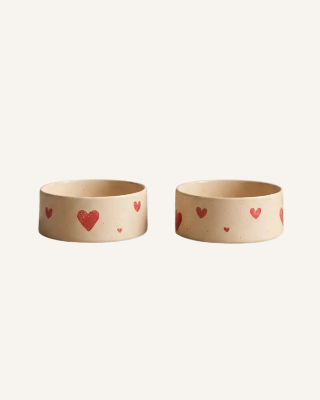 Two beige ceramic pet bowls decorated with small red and brown hearts.