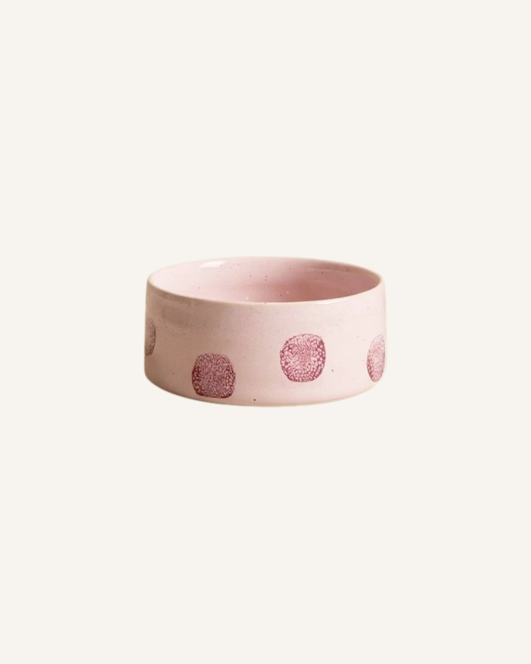Round pale pink ceramic pet bowl with raised dusty rose dot decorations around the exterior.