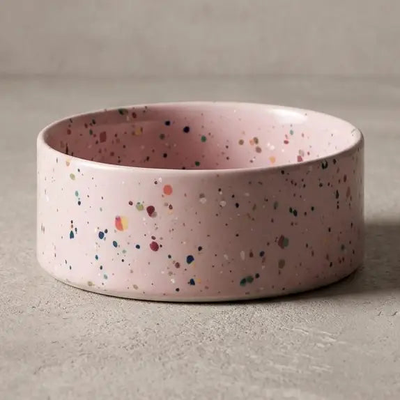 Pink ceramic pet bowl with multicolored speckled design, low and round shape.