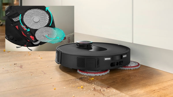 Black Bosch BCRDW3BX robot vacuum with dual spinning mop pads cleaning hardwood floor near white wall.