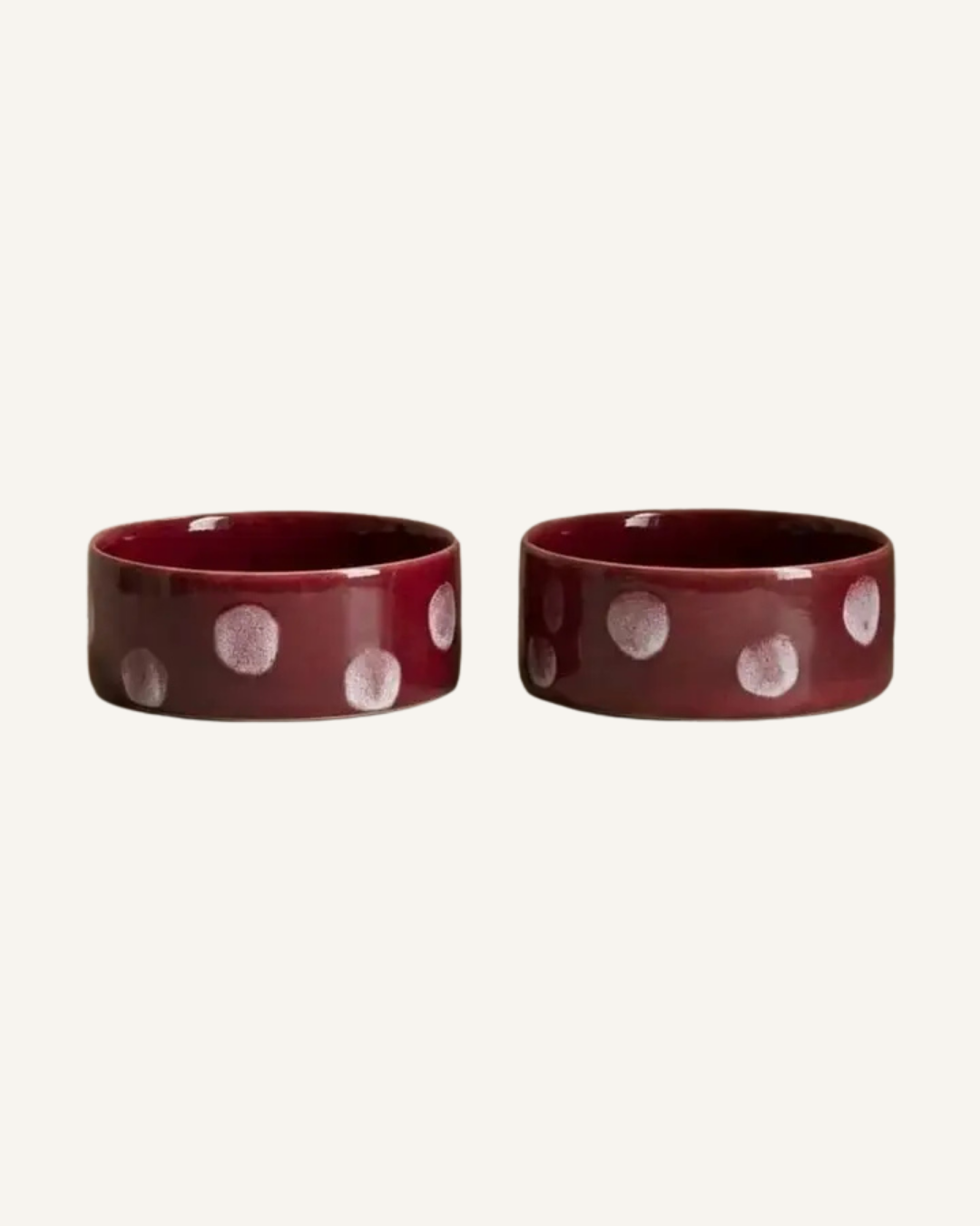Two burgundy ceramic pet bowls with a glossy finish and raised white dot accents.