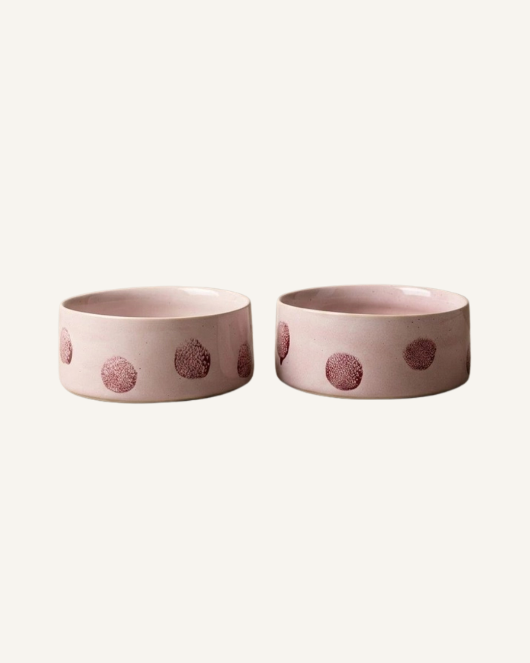 Pair of pink ceramic pet bowls with a low rounded shape and raised textured dot pattern.