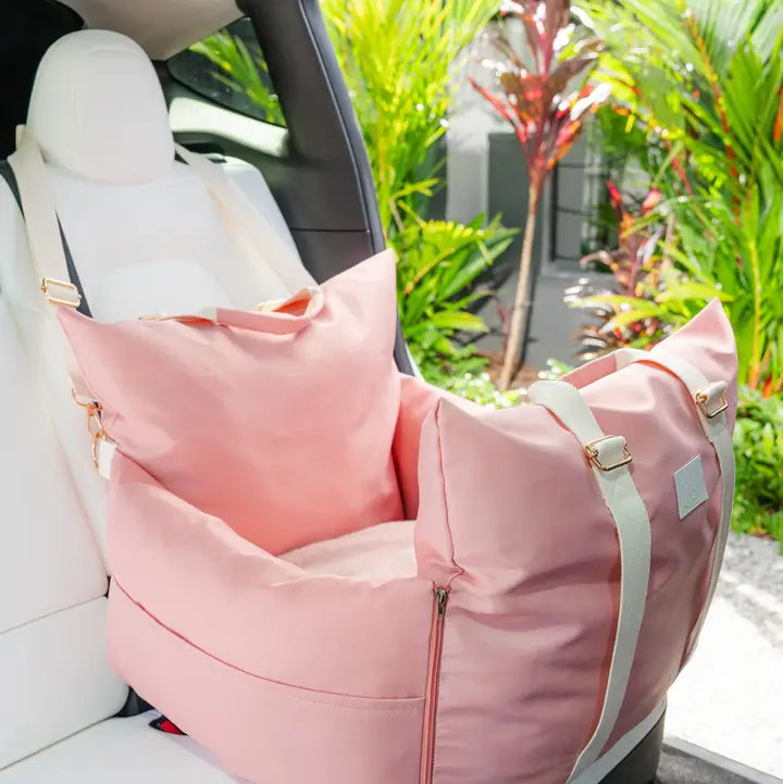 Pink pet car seat with adjustable straps and padded interior on white car seat.