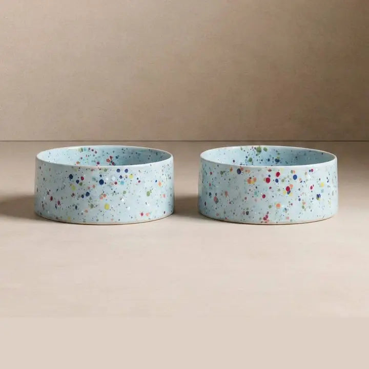 Set of two light blue ceramic pet bowls with multicolored speckled design, 16.5 cm diameter.